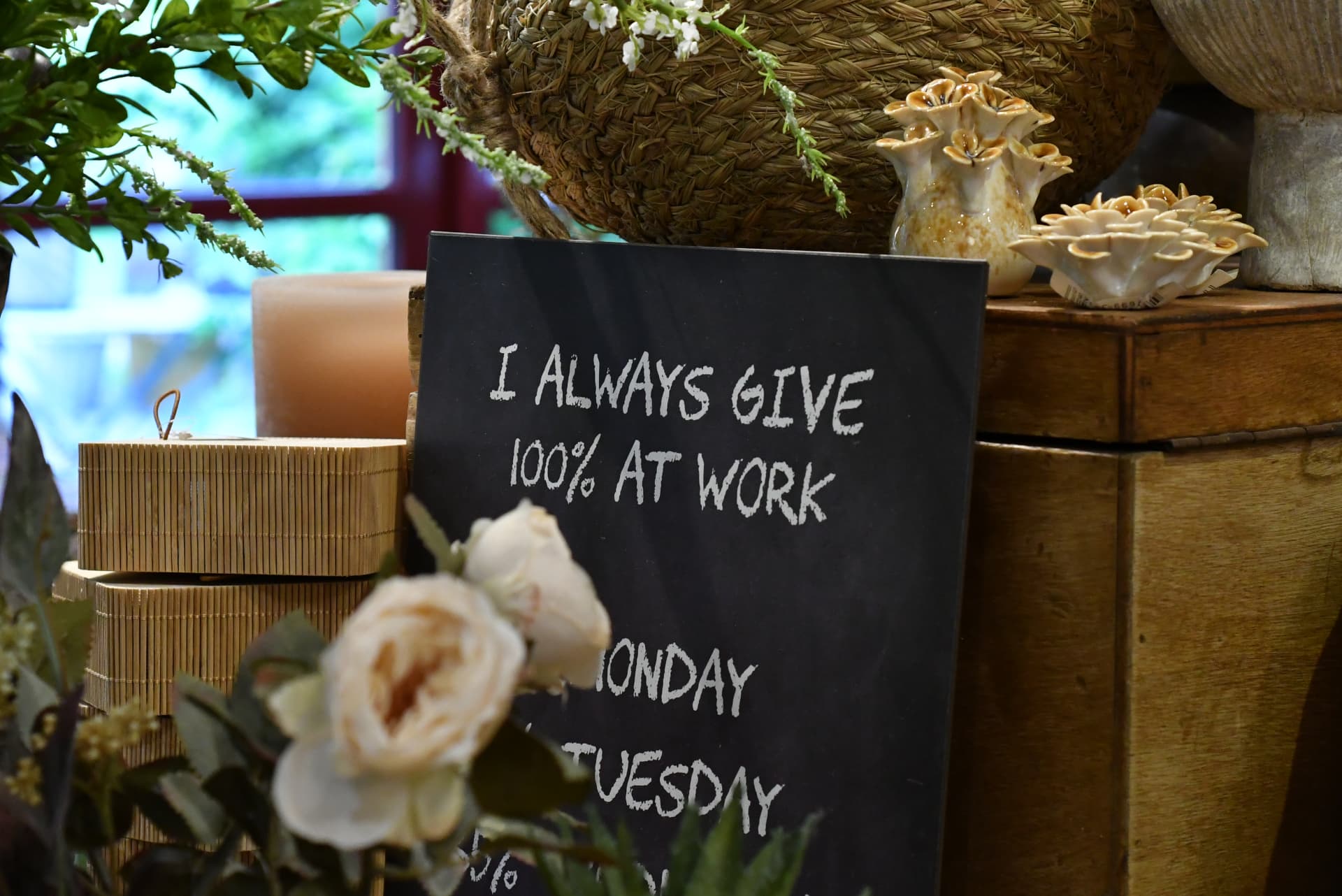 Tavle med teksten 'I always give 100% at work' mellem kurve, lys og keramik i butikken