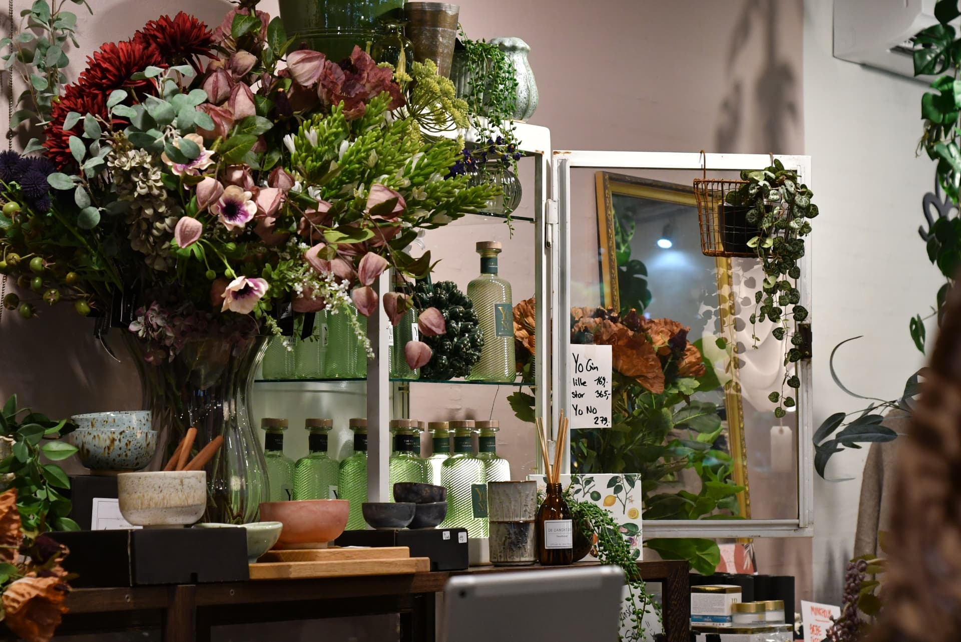 Blomster, keramik og Yo Gin-flasker i vitrineskabet i butikken